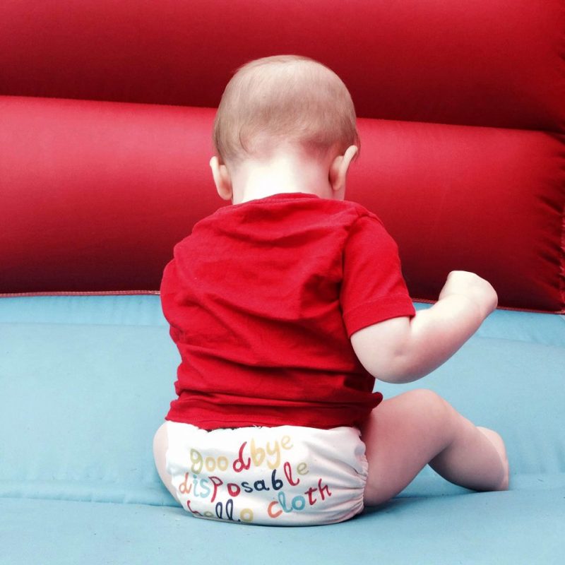 cloth nappies to go waste free Toddler sitting on a bouncy castle wearing a reusable nappies that says "Goodbye disposable, Hello Cloth"